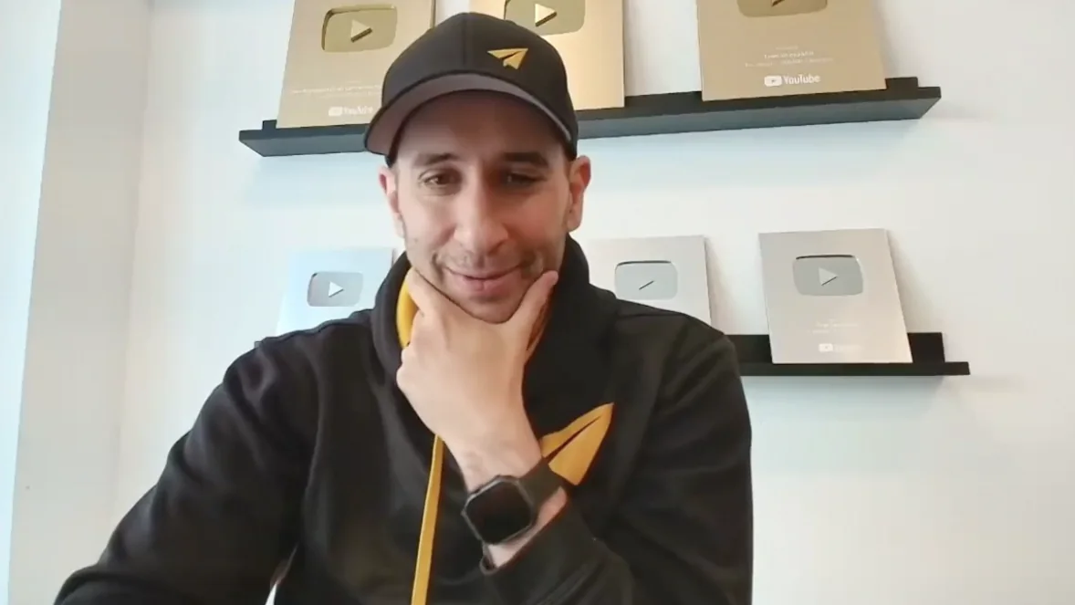 Evan Carmichael on a video call, hand on chin, reviewing a screen; behind him two shelves of gold and silver YouTube Play Button plaques